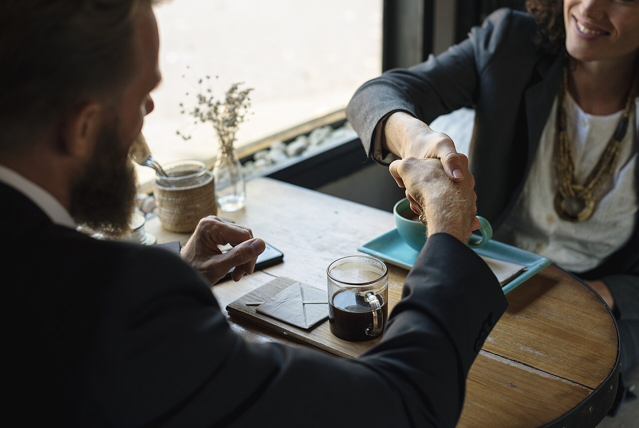 Two people shaking hands across a coffee shop table